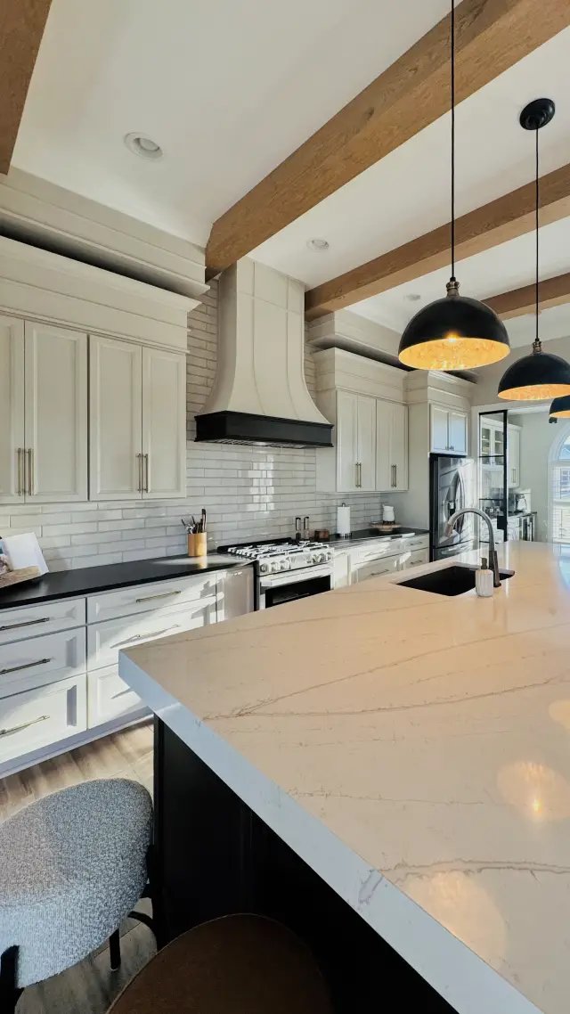 Oyster perimeter cabinetry with a Black island under a beamed ceiling